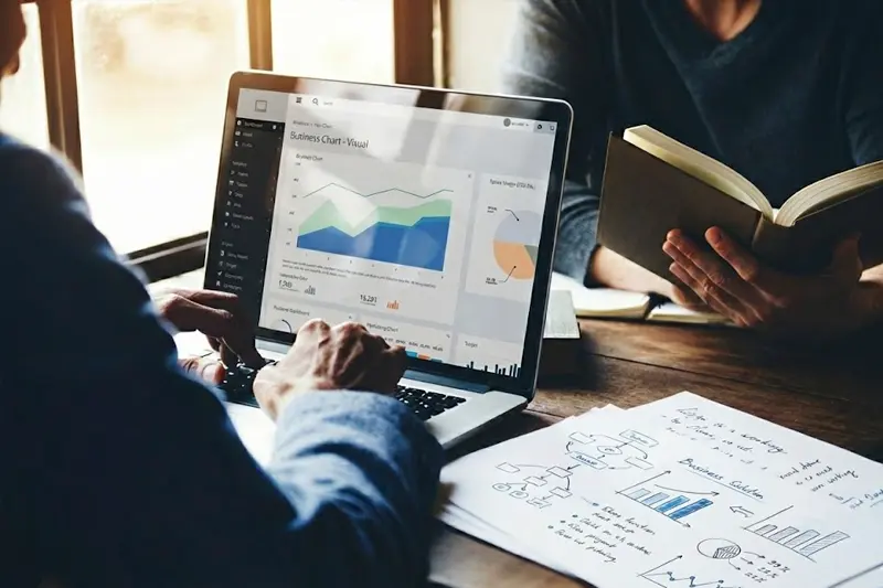 Escritorio de trabajo en agencia SEO mostrando la fusión entre analítica de datos en monitor y estrategia creativa manuscrita en libreta sobre autoridad y confianza (EEAT)