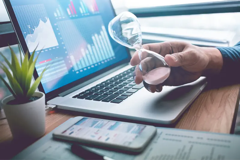 Análisis de auditoría SEO en un portátil con gráficas, y una mano sosteniendo un reloj de arena que simboliza el tiempo y los clientes perdidos.